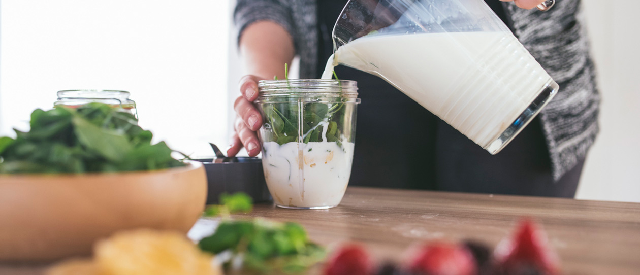 Woman making a smoothie with milk and spinach