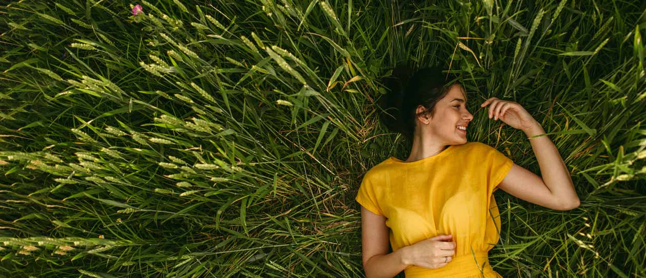 Smiling woman in a yellow dress lying in grassy meadow
