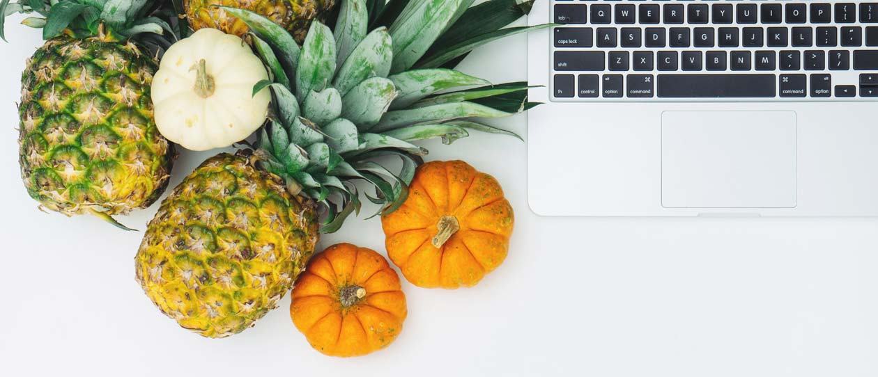 Pineapple, pumpkin and a mac book laptop on a white background