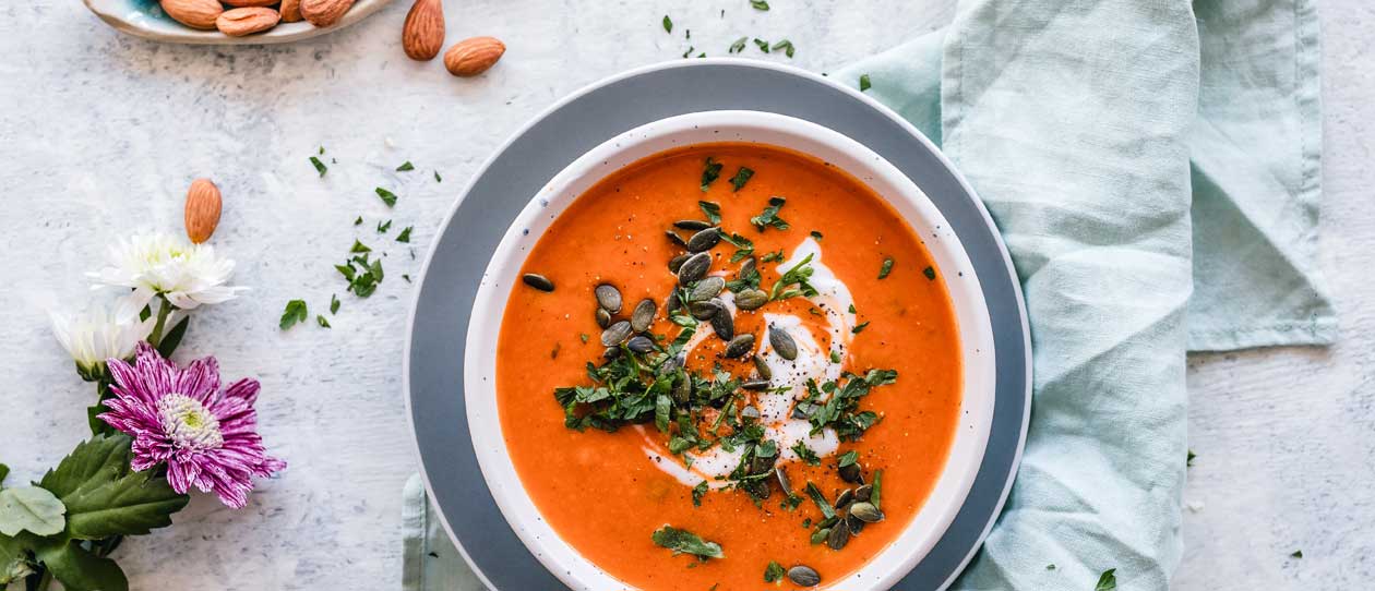 Tomato and carrot soup in a bowl with pumpkin seeds and almonds