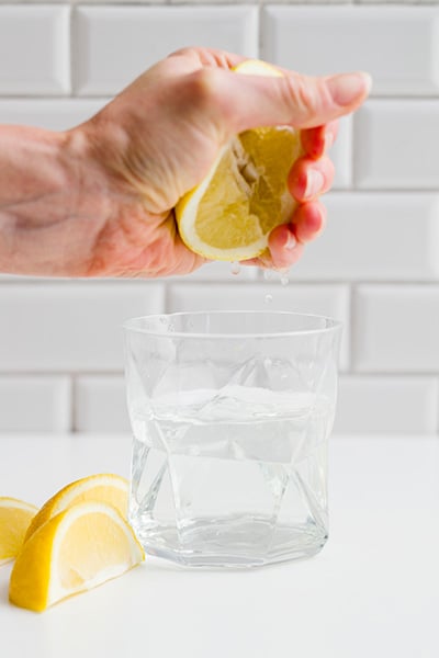Squeezing fresh lemon juice by hand into a glass of water