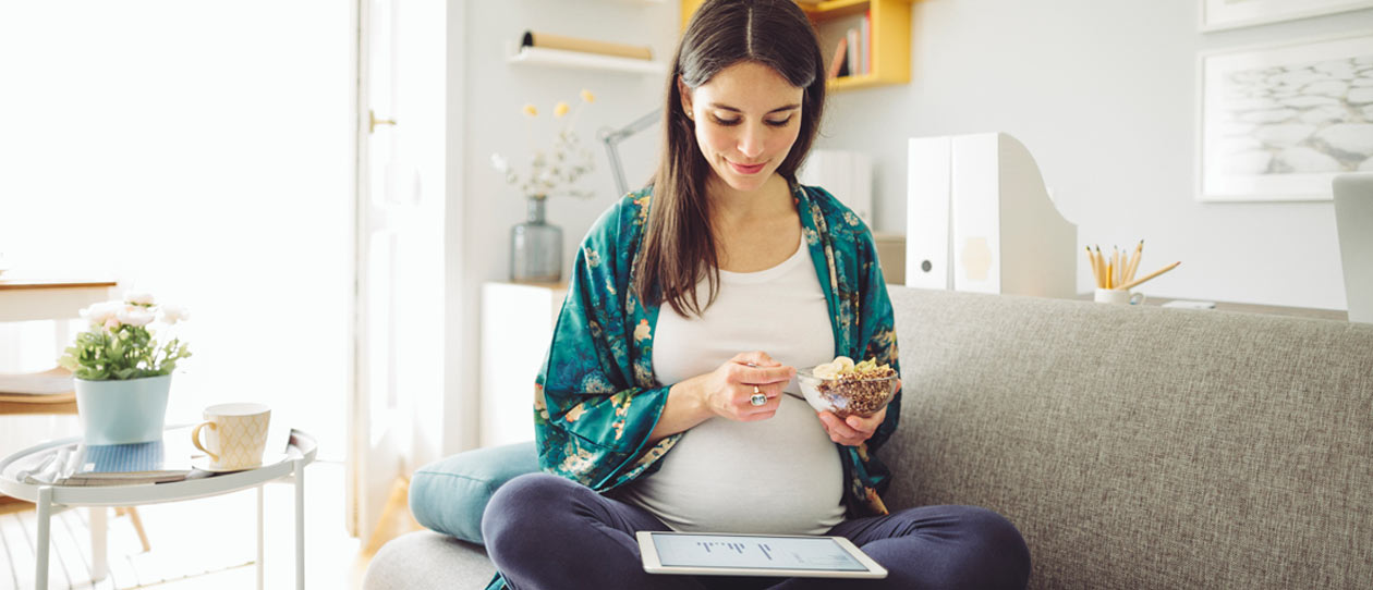 Pregnant woman sitting on the couch at home eating cereal