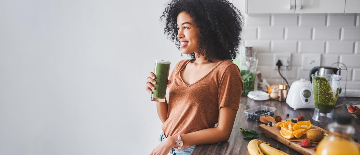 Woman leaning against the kitchen counter drinking a green smoothie