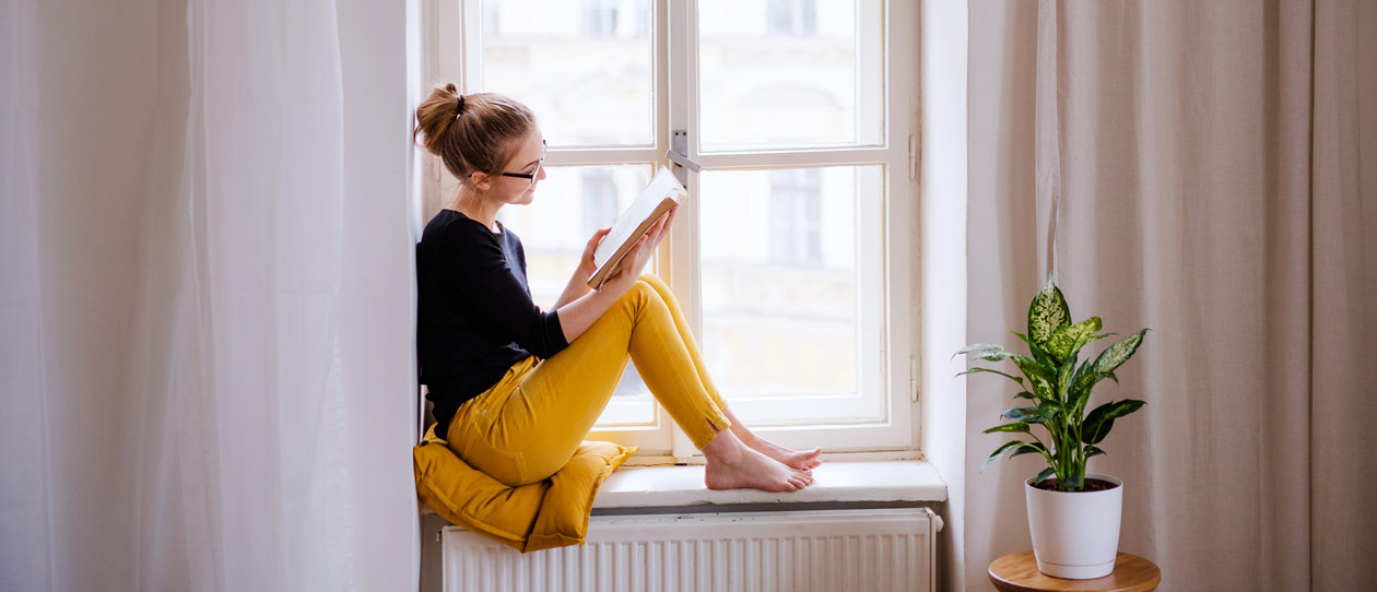 Young woman sitting in a sunlit windowsill reading a book