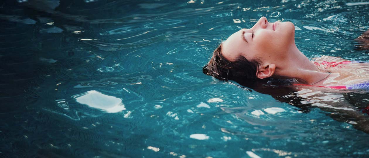 Woman relaxing and floating on water in sunlight