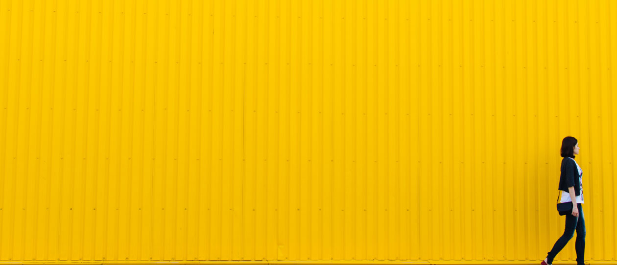 Young woman walking in front of a yellow wall