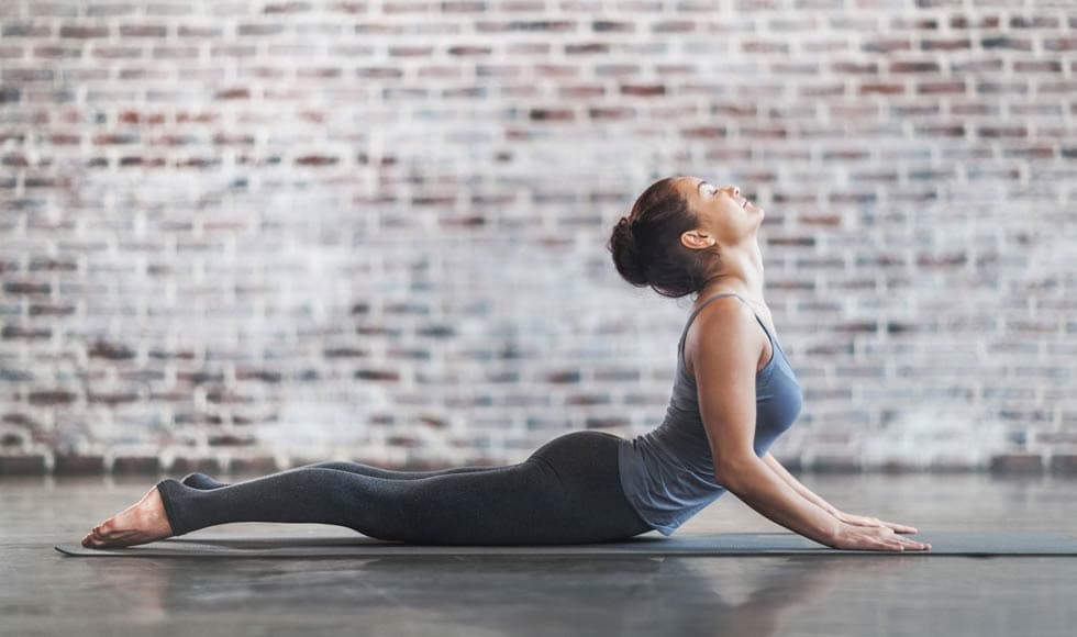 Young woman doing an upward facing dog yoga pose on a grey yoga mat