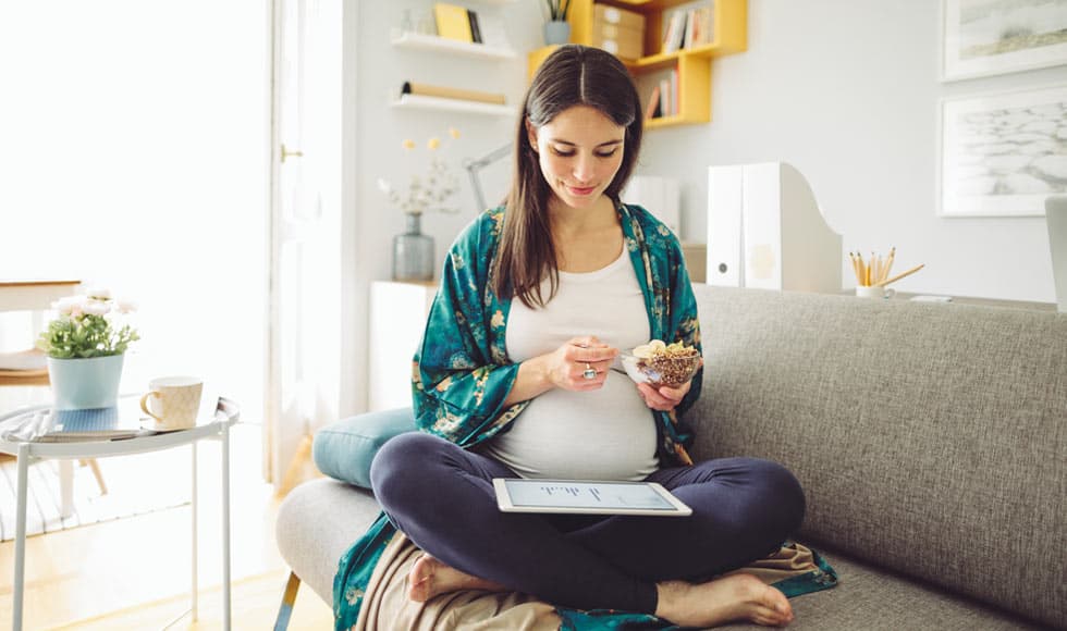 Pregnant woman sitting on the couch at home eating cereal