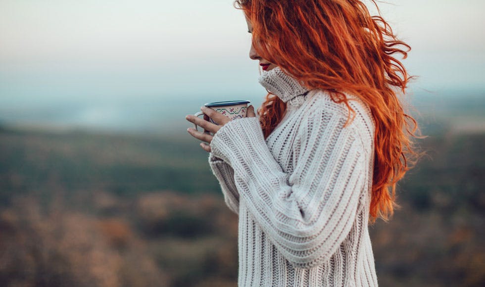 Young woman with bright red hair sipping a hot drink on a cold day outside
