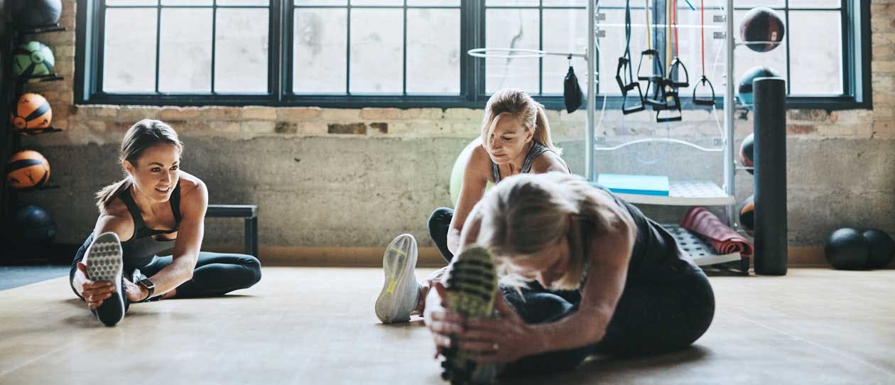 Three women stretching in the gym with lots of exercise equipment around them