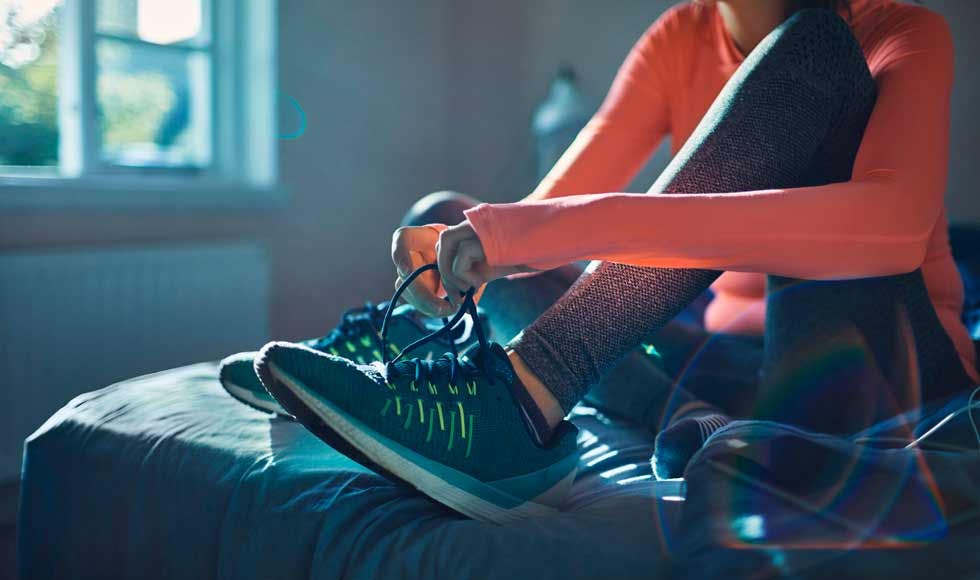Woman sitting on her bed putting running shoes on