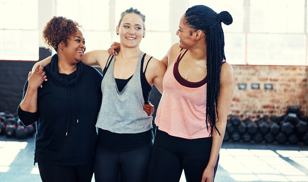 Three happy women having a conversation while holding each other before a workout session in a gym