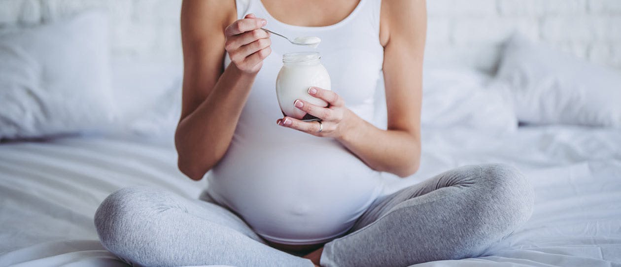 Pregnant woman sitting on the bed eating yoghurt
