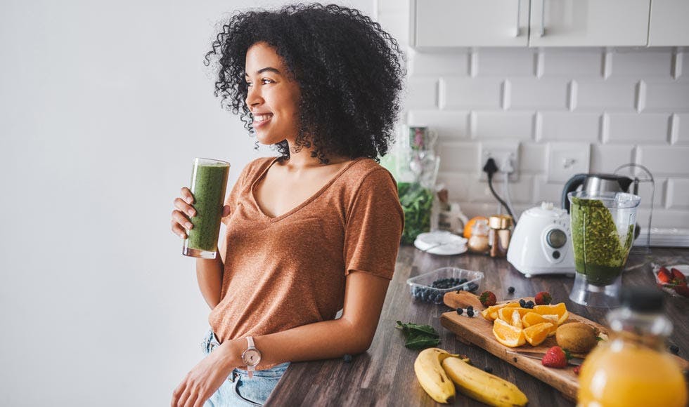 Woman leaning against the kitchen counter drinking a green smoothie