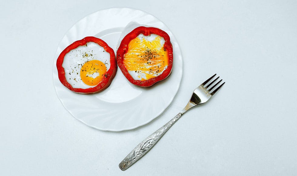 Bright and juicy picture with orange eggs and red capsicum. The eggs are on a plate, next to the plate there is a fork.
