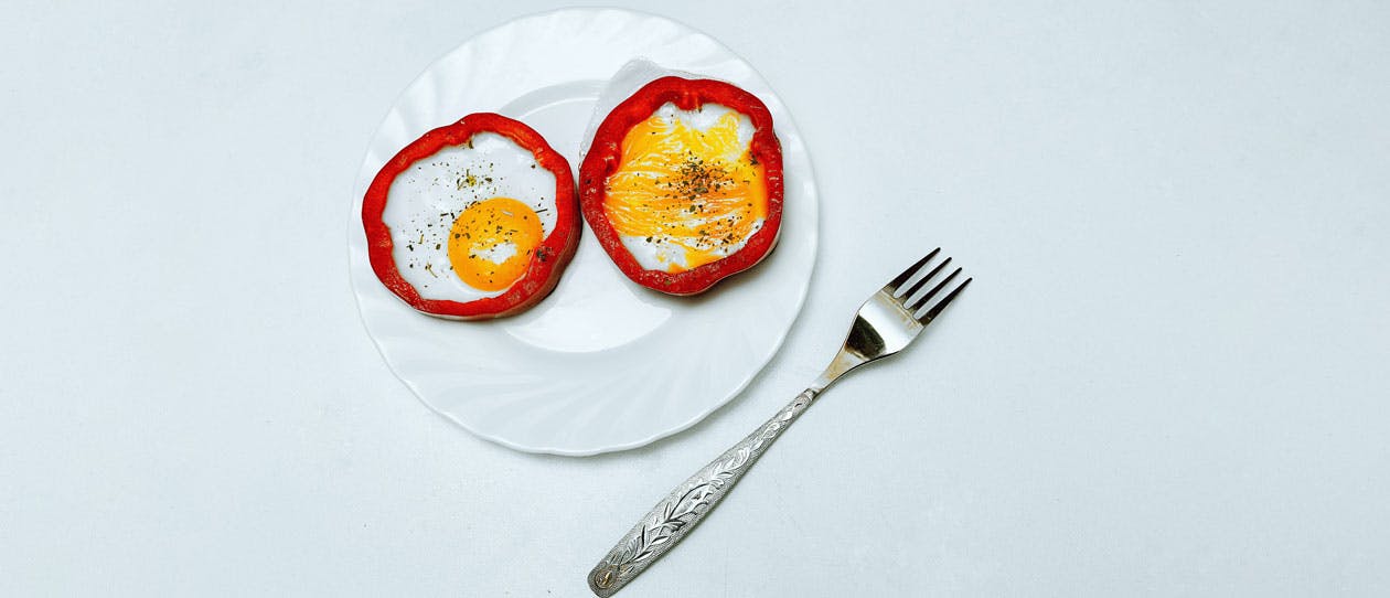 Bright and juicy picture with orange eggs and red capsicum. The eggs are on a plate, next to the plate there is a fork.