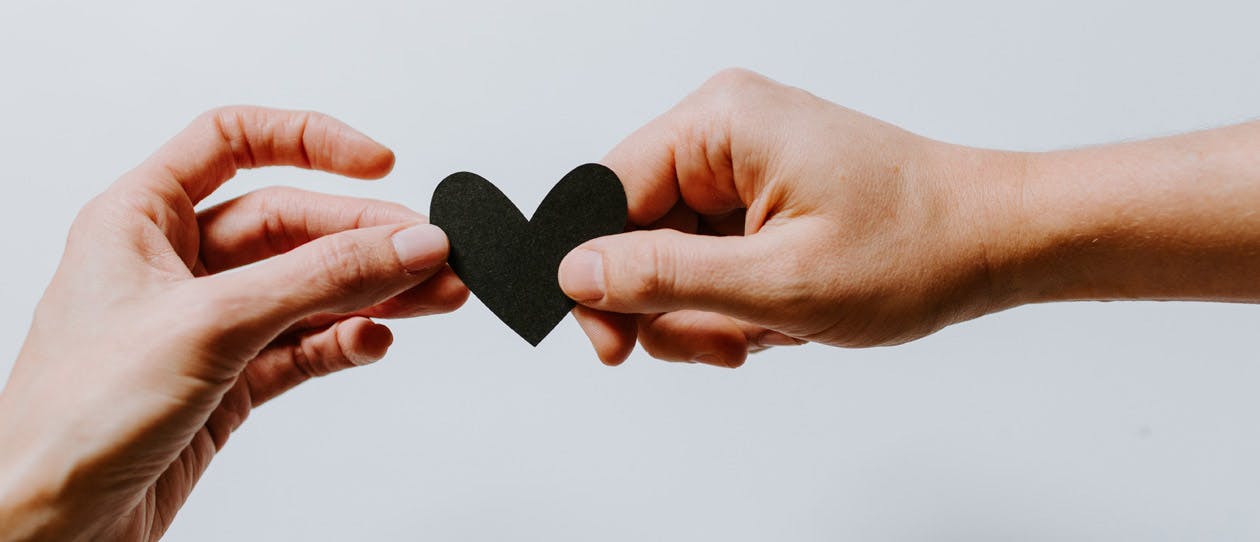 Two hands holding a black paper heart