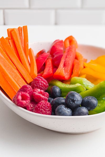 Bowl of fresh raw vegetables and berries on a white bench top
